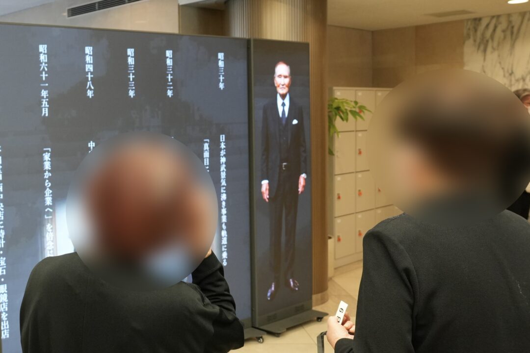AI技術で再現された故人の映像に見入り、その歩みをあらためて感じ取る参列者たち。